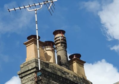 Brick chimney stack with various clay chimney pots alongside a rooftop TV aerial mounted on a slate roof