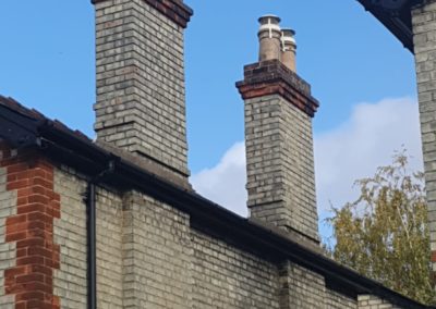 Two tall brick chimneys with cowls on residential roof