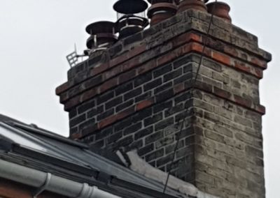 Brick chimney with multiple chimney pots and caps on a tiled roof